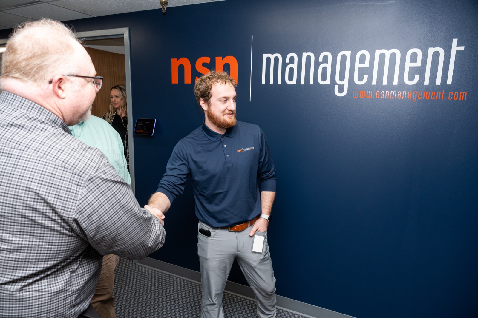 A handshake in front of the NSN Management logo wall